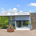 Vue extérieure de l'entrée du magasin AQUALSACE à Sarreguemines, avec une grande enseigne 'PISCINE - SPA - SAUNA'. La façade moderne présente une grande vitrine permettant de voir les produits exposés à l'intérieur, dans un environnement urbain avec un parking accessible à l'avant.