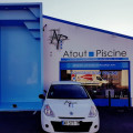 Façade du magasin Atout Piscine à Lézignan Corbière avec un grand panneau bleu affichant le modèle de piscine exposé à l'extérieur. L'enseigne du magasin indique 'Vente - Construction - Entretien - SAV' avec des informations de contact visibles, reflétant un espace professionnel dédié aux piscines.