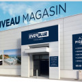 Façade du magasin BE SPA Lorp-Sentaraille - Azur Piscines Everblue avec des grands logos et enseignes visibles. La façade blanche est décorée de visuels de piscines avec des montagnes en arrière-plan sur une grande bannière, promettant 'Excellence & Sérénité' aux visiteurs, située dans une zone industrielle avec un parking en gravier à l'avant.