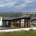 Le magasin Audigier Piscines à Aubenas, avec une architecture moderne en verre et bois, offre une vue panoramique sur le paysage montagneux environnant. Situé dans un cadre commercial, le bâtiment présente une grande visibilité avec son enseigne lumineuse et ses larges vitrines exposant divers produits pour piscines et spas