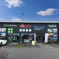 Façade moderne du magasin BE SPA BCF HABITAT à Laval, partageant le bâtiment avec d'autres entreprises telles qu'Art & Fenêtres et Brisach. Le magasin est facilement identifiable grâce à son grand logo 'be spa' visible au centre, entouré de publicités pour divers produits de bien-être et constructions, dans une zone commerciale active avec un parking accessible.