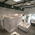 Showroom du magasin BE SPA BCF HABITAT à Laval, partageant le bâtiment avec d'autres entreprises telles qu'Art & Fenêtres et Brisach. Le magasin est facilement identifiable grâce à son grand logo 'be spa' visible au centre, entouré de publicités pour divers produits de bien-être et constructions, dans une zone commerciale active avec un parking accessible.