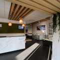 Intérieur du showroom BE SPA CONCEPT LE MANS NORD à Saint-Saturnin avec une réception moderne et des jacuzzis exposés. Le design est épuré avec des poutres en bois, un mur végétal et des lampes suspendues élégantes. La réception en marbre blanc affiche le logo 'be spa', créant un environnement accueillant pour les clients.