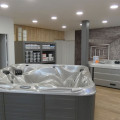 Intérieur du showroom Concept Spa à Marly, exposant divers modèles de jacuzzis et spas de nage. La pièce est spacieuse avec un sol en bois laminé, des murs décorés de bois clair et de briques, et des étagères de produits d'entretien. L'éclairage moderne et la présentation élégante mettent en valeur les spas disponibles pour la vente.