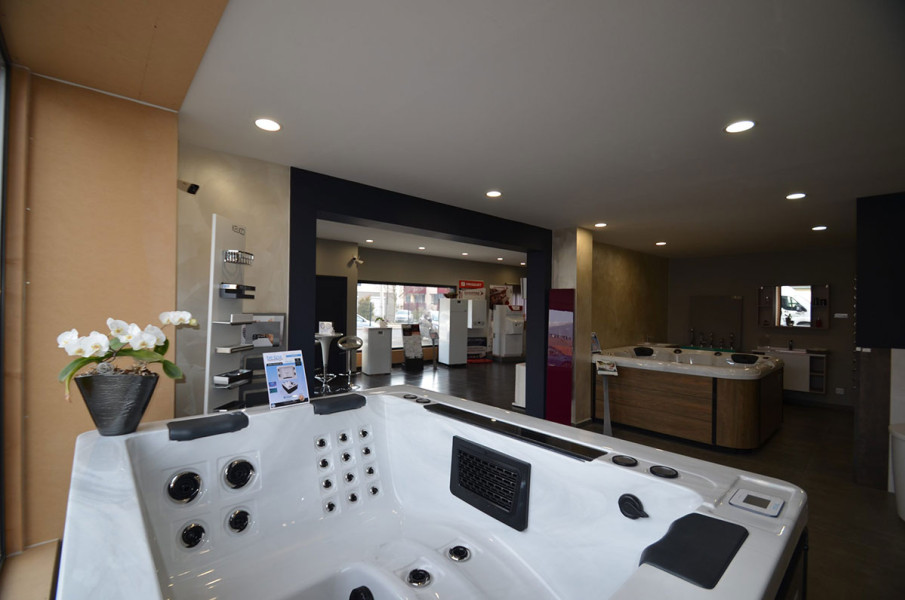 Vue intérieure du magasin Bournonville à Cessy, présentant un spa BE SPA luxueux au premier plan. L'arrière-plan montre un espace d'exposition vaste et bien éclairé avec d'autres modèles de spas et une réception. La décoration moderne et les accessoires élégants comme les orchidées blanches sur le comptoir ajoutent une touche d'élégance et invitent à la relaxation.