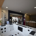 Vue intérieure du magasin Bournonville à Cessy, présentant un spa BE SPA luxueux au premier plan. L'arrière-plan montre un espace d'exposition vaste et bien éclairé avec d'autres modèles de spas et une réception. La décoration moderne et les accessoires élégants comme les orchidées blanches sur le comptoir ajoutent une touche d'élégance et invitent à la relaxation.