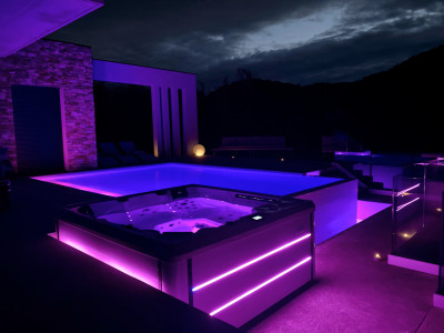 Spa Blue Bay installé sur une magnifique terrasse, éclairé par des bandeaux LED programmés en violet qui soulignent le contour du jacuzzi, créant une atmosphère élégante et relaxante pour une soirée de détente extérieure