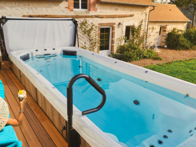 Image d'une femme allongée détendue sur une chaise longue sur une terrasse, à côté d'un spa de nage. La scène dépeint un moment de relaxation en plein air, avec la femme profitant du soleil et de la tranquillité environnante, évoquant un style de vie sain et relaxant.