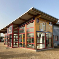 Vue extérieure de La Boutique du Menuisier - 123 Menuiseries située au 262 rue Pierre et Marie Curie, 01400 Chatillon-sur-Chalaronne. Façade moderne avec structure en bois et encadrements rouges, offrant divers produits de menuiserie et des spas BE SPA